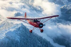 A red airplane flying over a snowy mountain range photo