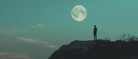 A man standing on top of a mountain with the moon in the background photo