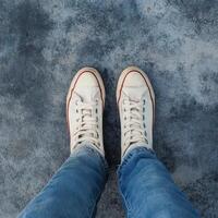 A person wearing white sneakers standing on a concrete floor photo