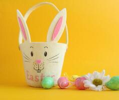 On a yellow background there is an egg basket in the shape of a rabbit and Easter decorative eggs photo