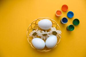 A wicker plate with decorative Easter eggs stands on a yellow background. photo