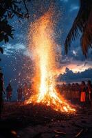 Beach bonfire at night. Large fire burns as people watch. Ocean and clouds in the background. Bright flames and sparks in the air. photo