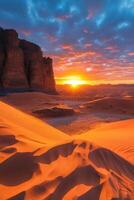 Desert sand dunes. Sun shines above land. Orange sand and blue sky. Mountain sits at edge of dunes. photo