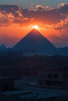 Pyramid at Sunset. Sun shines above big ancient pyramid. Red and orange sky with clouds. Dark landscape in front. Travel background. photo