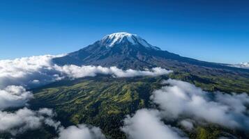 Mountain peak with snow. Green trees below. White clouds surrounding. Clear blue sky. Natural landscape. Aerial view. High altitude scenery. Mountain top. photo