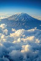 Snowy mountain peak rises above the clouds. Blue sky above. Mountain top view with white puffy clouds and soft light. Landscape nature aerial view. photo