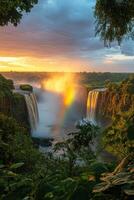 Waterfall view at dawn. Lush green plants around water. Mist and rainbow form by waterfall. Colorful light on sky. Natural wonders. photo