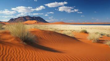 Desert landscape. Sand dune shows ripple pattern. Lake shines in the background. Plants grow beside the dunes. Distant mountain visible. Blue sky has fluffy clouds. photo