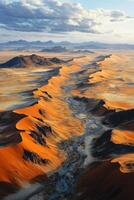 Desert Sand Dunes View. River Through Sand. Golden Light on Landscape. Mountain Range in Distance. Scenic Desert Vista From Above. Cloudy Sky. photo