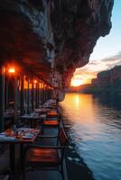 River view restaurant. Tables set up for dinner. Evening light reflects on the water. Rock overhang above the dining space. photo