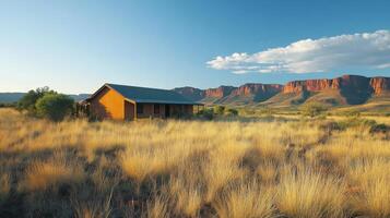 Old house stands in dry grass. Distant mountains under blue sky. Landscape shows nature and building in field. Desert plain with open view. photo