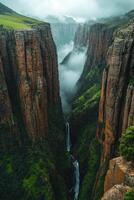Tall canyon with waterfall. Cloudy sky over steep rocks. Green grass on cliff face. Scenic view of landscape with natural mountain valley. photo