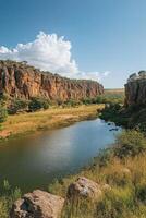 River flows between tall rock walls. Beautiful blue sky with white cloud above. Green trees line the landscape. Grass grows on the river edge. photo
