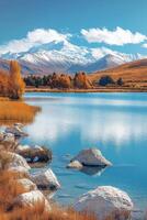 Mountain lake view. Blue water with rocks in foreground. Autumn colors with snow covered mountain. Peaceful lake under bright sky. photo