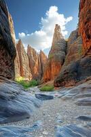 Canyon view with tall rock formations. Dry river bed in foreground. Blue sky and white clouds above. Rocks are gray and orange. Sunlight shines through gap. photo