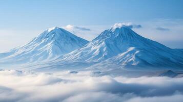 Two snowy mountains rise above white clouds under a clear blue sky. A peaceful winter landscape with sunshine and fog. photo