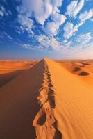 Sand dune in desert. Footprints in sand lead away. Blue sky and white clouds above. Warm orange color. Journey and adventure concept. photo