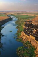 River flows through grassy landscape near ancient ruins. Water stream winding through fields with buildings ruins visible. Countryside scene with horizon in background. photo