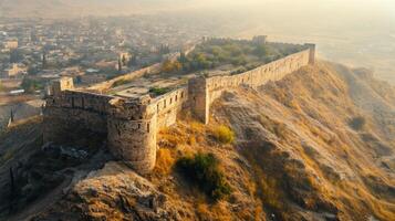 Ancient stone wall on hilltop. Castle walls overlooking town. Old fortress on a hill. Cityscape behind old wall. Warm light on stone structure. photo