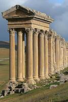 Old stone building. Row of pillars stand tall. Temple ruins on hillside. Architecture and sky. Historic building with many columns. photo