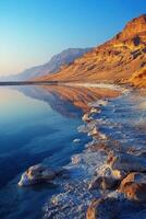 Lake view near mountains at sunrise. Water reflects hills on bright day. Shoreline shows salt and rocks at edge. photo