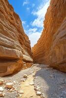 Desert canyon landscape. Tall rocks form a narrow path. Water flows on small pebbles. Bright sky is visible between rock formations. photo