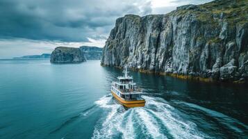 Yellow boat sails on blue ocean near rocky cliffs. Grey clouds above. Water trail behind boat. photo