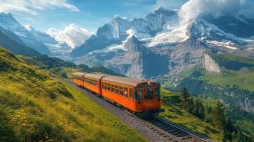 Mountain train travels through green hills. Snow covered peaks rise in background. Sunny day with blue sky and white clouds above train. photo