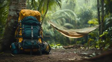 Backpack leans on tree in jungle. Hammock sways in background. Green plants surround gear. Vacation and escape into nature. photo