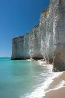 White cliffs meet blue sea. Waves reach sandy beach under clear sky. Peaceful coast with rocks and ocean. Coastal scenic view. photo