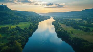 River flows between green hills. Water reflects sky light. Landscape shot from above. Nature scene shows peaceful valley. Serene view with trees. photo