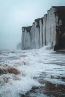Sea waves crash against white chalk cliffs on cloudy day. Water surging near shore with sea stacks on background. Nature scene. photo
