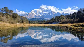 Mountain reflects on lake water. Trees grow near shore. Sky is blue with clouds. Peak is snow covered. Scenic place with peaceful nature. photo