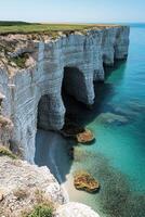 Ocean coast landscape. White cliffs extend into blue sea. Rocks and small beach seen from above. Clear water sparkles in sunlight. photo