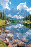 Mountain peak over clear lake. Trees surround water. Rocks sit underwater. Sky is bright blue with soft white clouds. Mountain reflects in water. photo