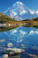 Snowy mountain reflects in lake. Rocks visible through water. Clear blue sky. Green and yellow grass on mountain side. photo