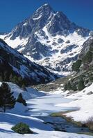Mountain peak covered in snow. Cold water in a small lake surrounded by rocks and trees. Scenic landscape on sunny day. photo