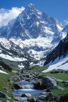 Mountain Peak View. Snow covers the mountaintop. A clear stream flows downhill. Green meadow and blue sky in background. Scenic landscape. photo