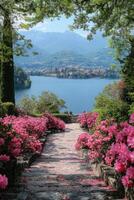 Stone path with pink flowers leading to calm lake view. Mountains and blue sky in background. Trees above the path. photo