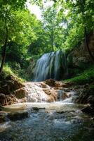 Waterfall in forest flows over rocks. Green trees surround the water. Cool water cascade landscape. Natural scenery with flowing stream. Scenic view outdoor. photo