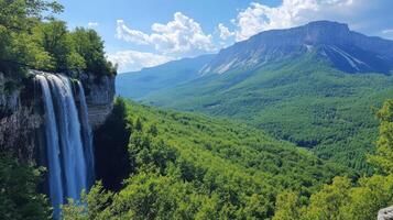 Waterfall cascades from cliff face into green forest valley. Mountain peak under blue sky with white clouds in background. Scenic nature landscape. photo