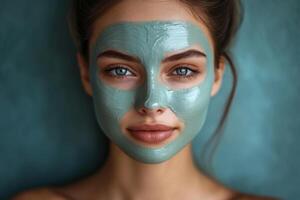 Close up of a woman with a green beauty mask on her face looking directly at the camera on a soft blue background photo