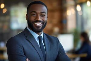 Confident man smiles with arms crossed in bright office. He wears a suit and tie. A woman works in the background. photo