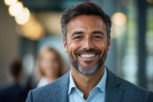 Close up of smiling man with beard wearing a suit in modern office setting. Two people are blurred in the background and light is soft. photo
