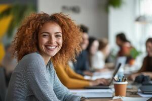 Smiling woman sits at a desk with coworkers. People work together in an office space. Natural light floods the room. photo