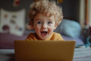 Small child with curly hair looks at laptop with surprised expression. Joyful face and open mouth. Warm sweater and blurred background. photo