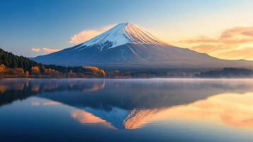 Snow covered mountain reflects in tranquil lake at dawn. Autumn trees line the shore. Mist rises from the water in peaceful landscape. photo