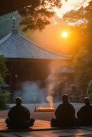 Three individuals meditate before a sacred fire at a Japanese temple as the sun rises casting warm light through the trees. photo