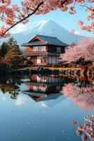 Japanese house near a lake with cherry blossom trees and a snow mountain backdrop reflecting on water in spring on a sunny day photo