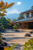 Zen garden with raked sand and rocks near a building and trees. A large mountain with snow stands in the distance under a blue sky. photo